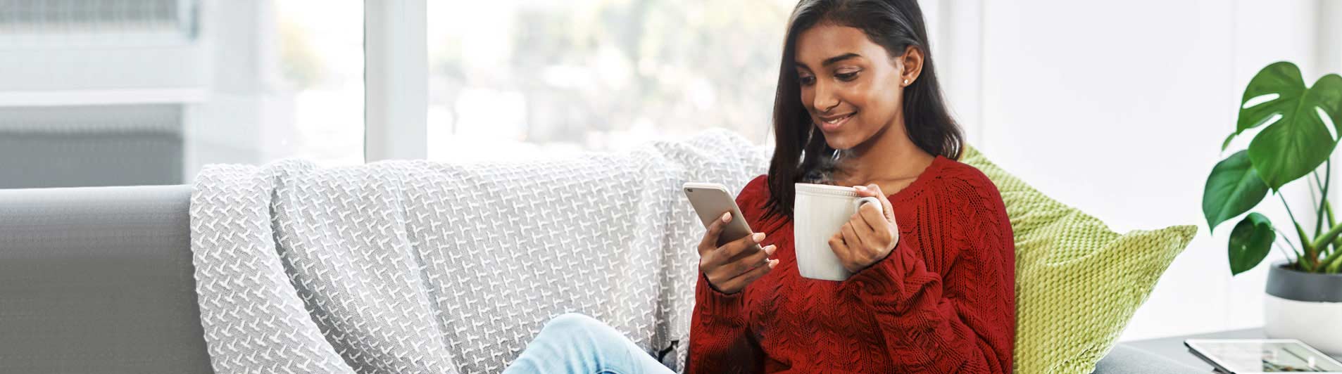 young woman sitting on couch while viewing mobile phone