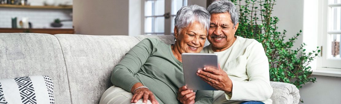 senior couple sitting on couch viewing a tablet together